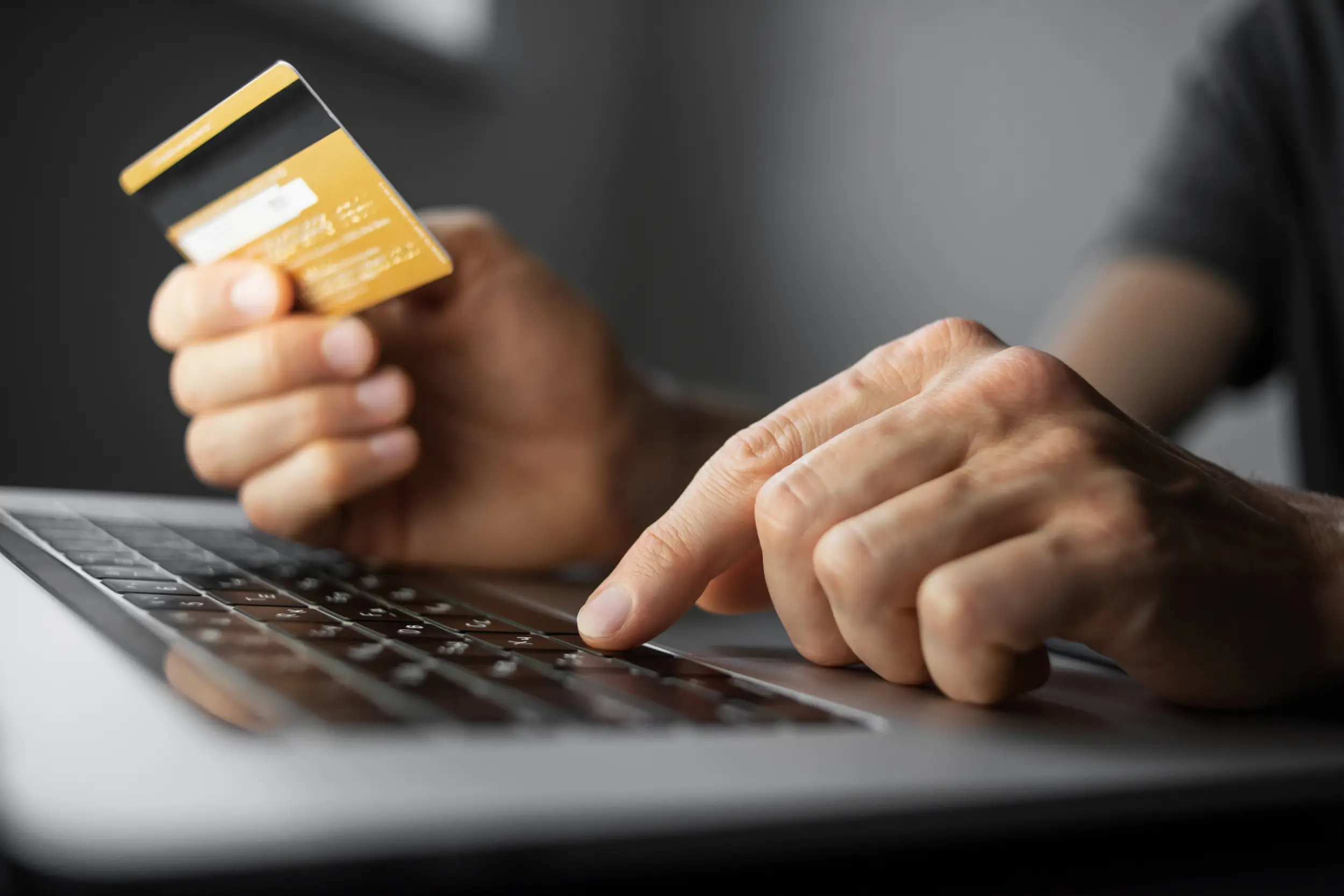 Eine Hand hält eine Kreditkarte, während die andere auf einer Laptop-Tastatur tippt, was auf einen Online-Einkauf oder eine Online-Banking-Transaktion hinweist.